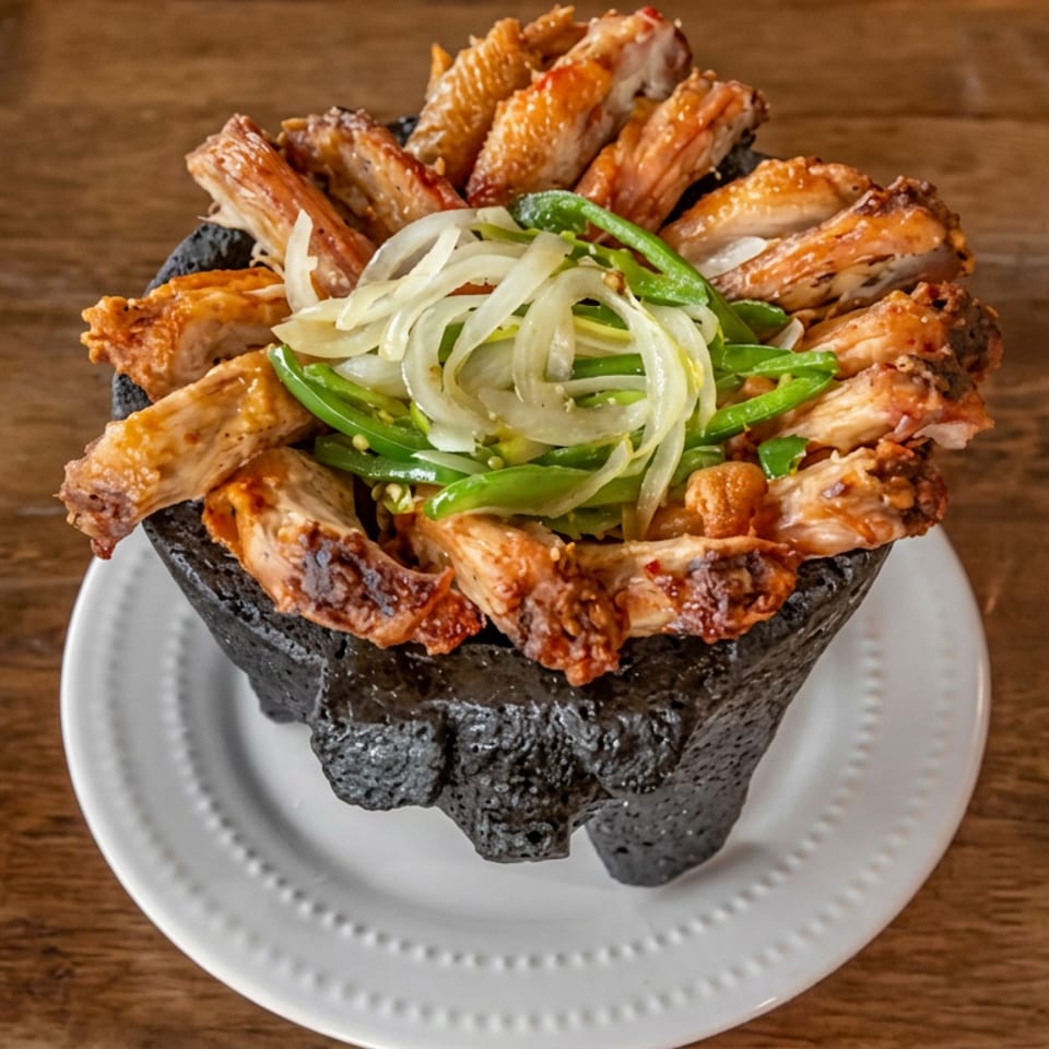 Crispy fried chicken wings arranged around sliced onions and green peppers in a black bowl on a white plate.